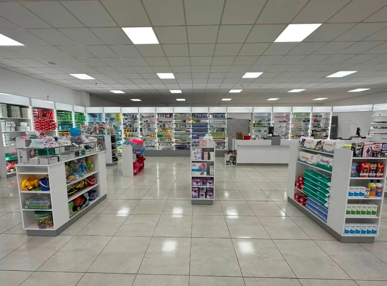 Salón de venta terminado con góndolas centrales y estanterías perimetrales en melamina blanca, mostrador de atención al fondo.