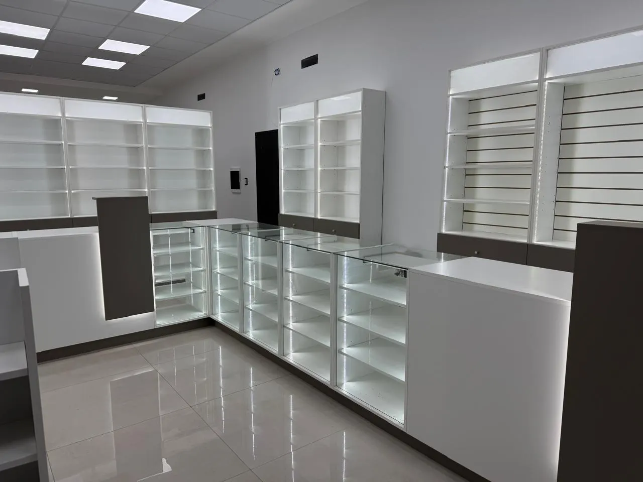 Mostrador de atención en L con estantería perimetral vidriada e iluminación LED.