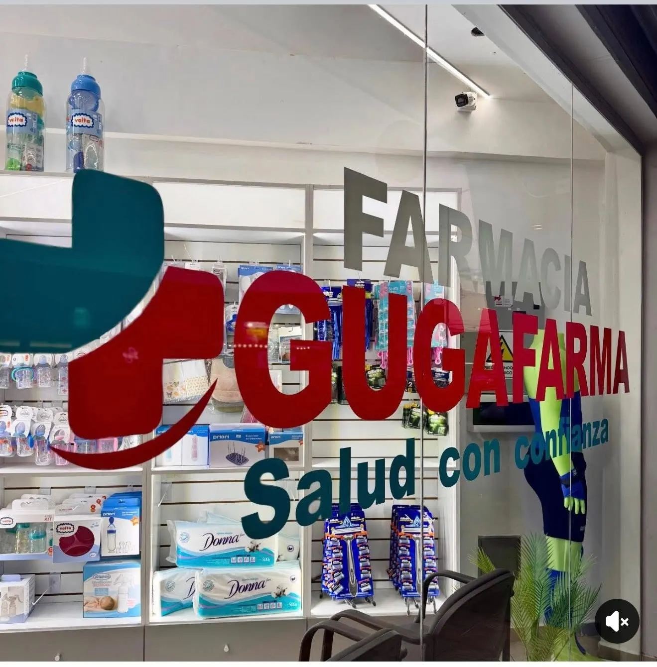 Detalle de la vidriera con el logo de Farmacia Gugafarma y estanterías de perfumería al fondo.