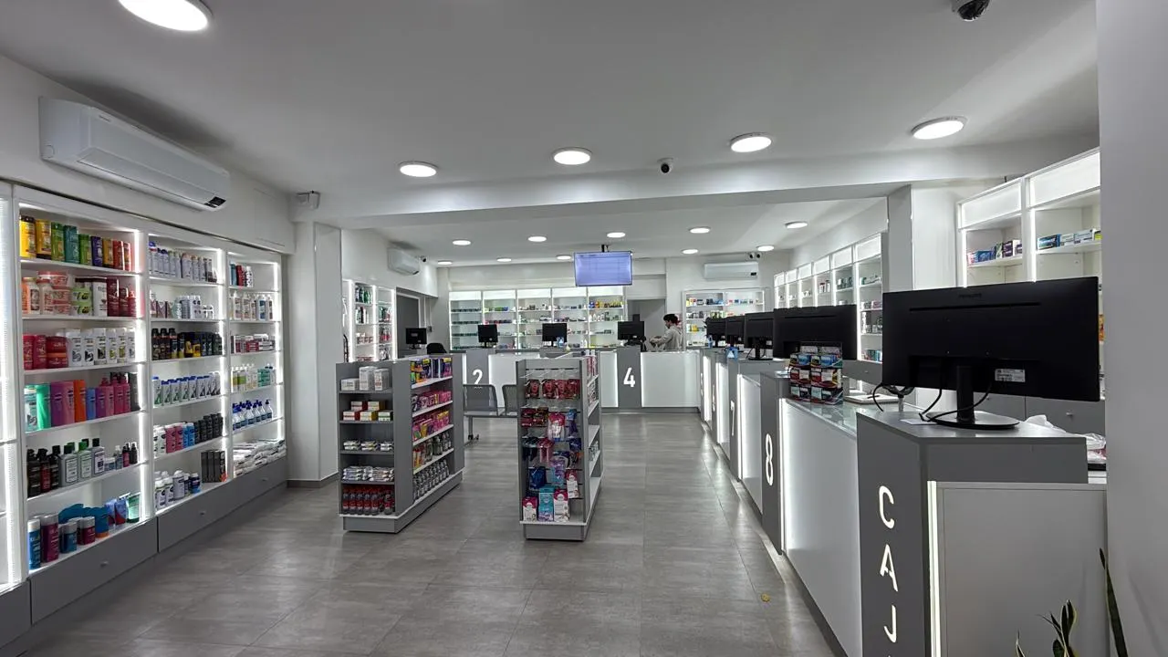 Salón de atención de Helios Salud con líneas de mostradores, puestos numerados y estantería perimetral en melamina blanca.