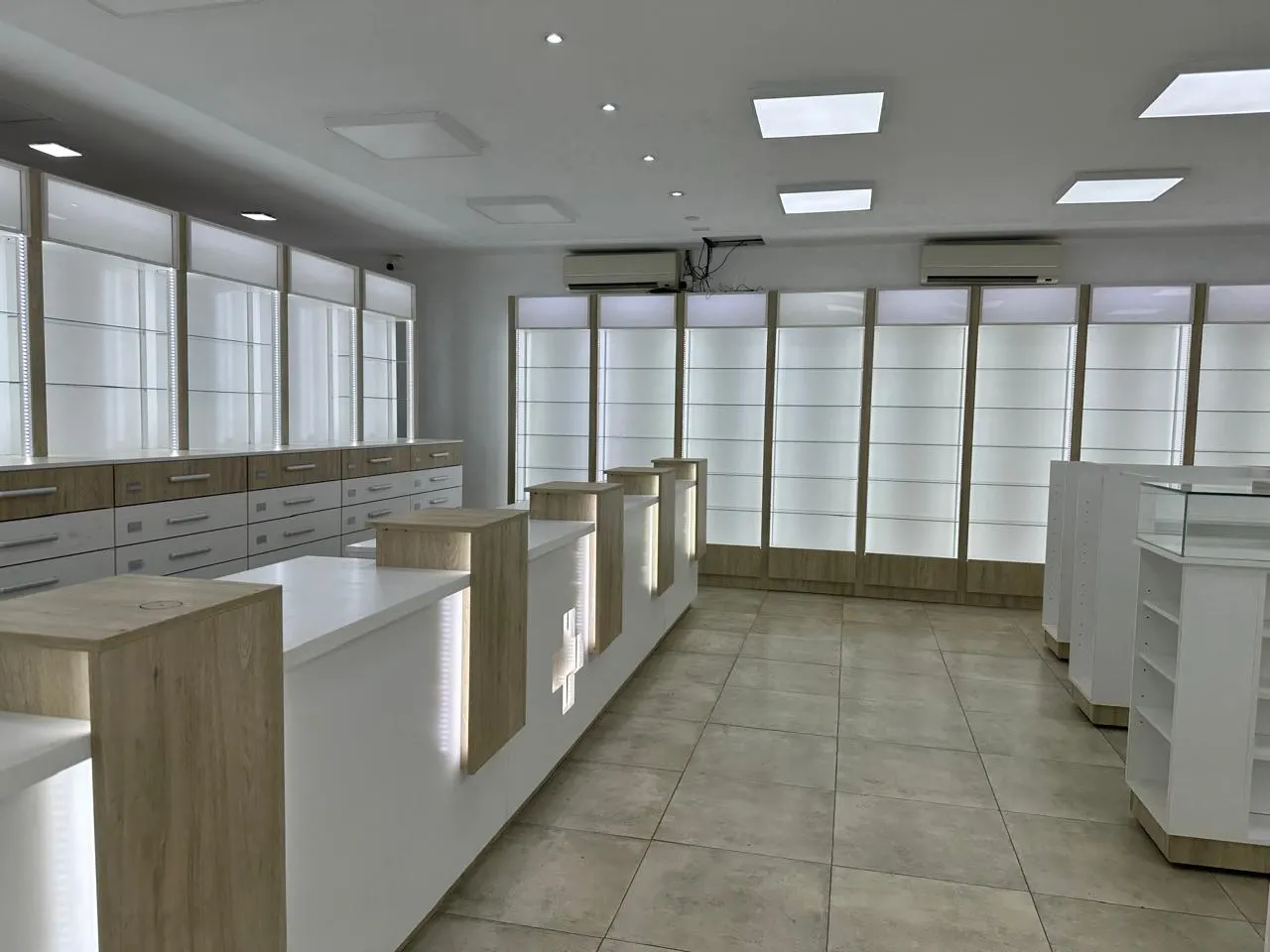 Mostrador de atención en blanco y melamina símil madera, con cruz farmacéutica retroiluminada en el frente.
