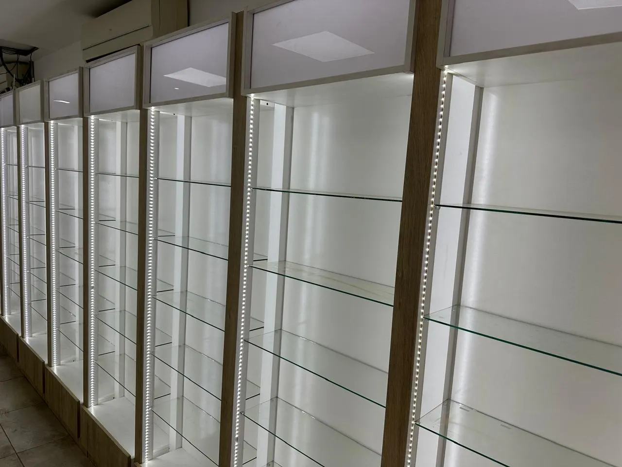 Mostrador en L con panel slatwall, repisas voladas y estantería esquinera iluminada.