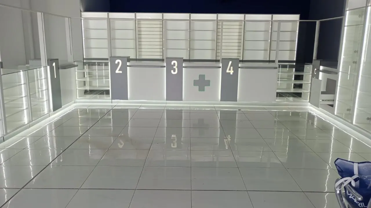 Puestos de atención numerados con cruz farmacéutica, estantería slatwall e iluminación LED, sobre piso blanco.