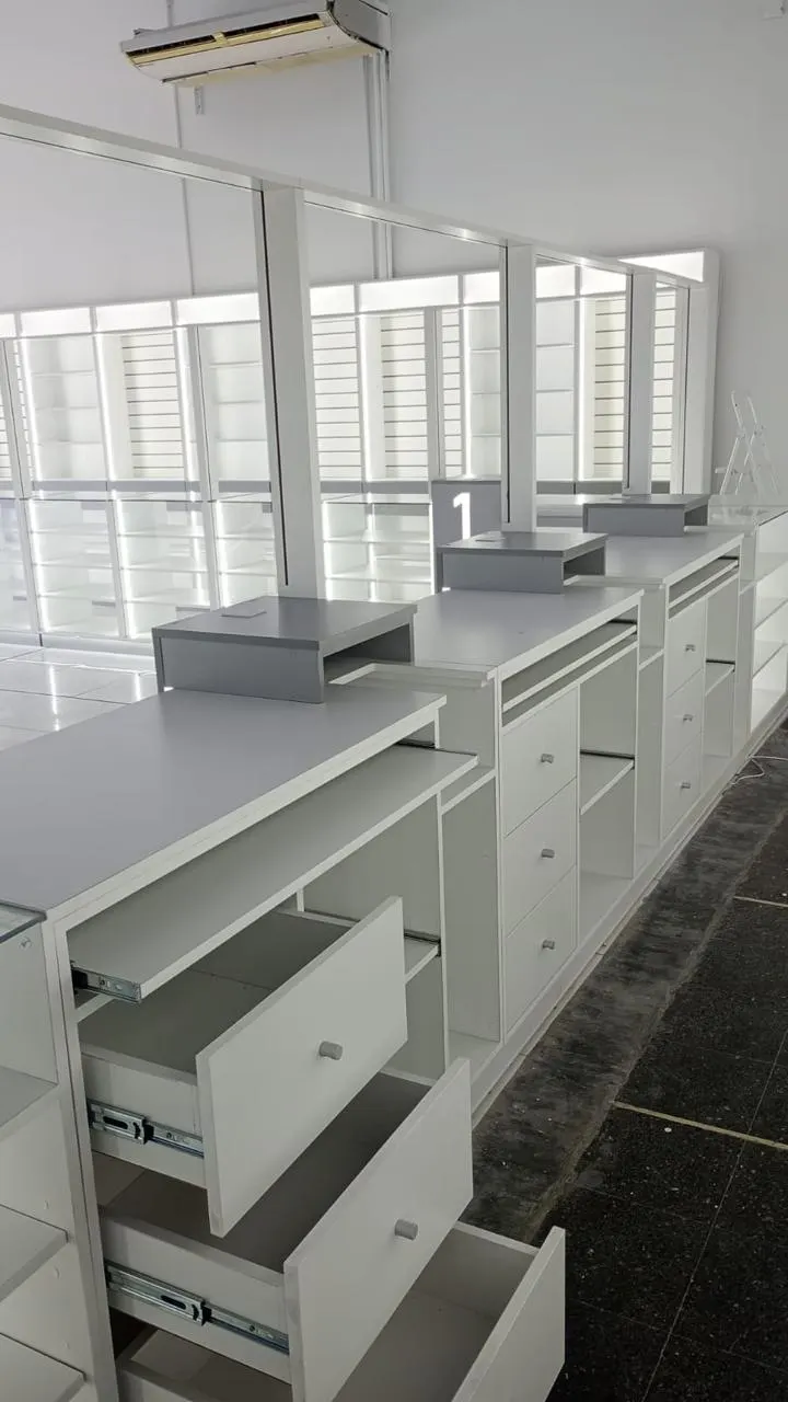 Línea de mostradores con cajoneras y repisas voladas numeradas, sobre piso oscuro.
