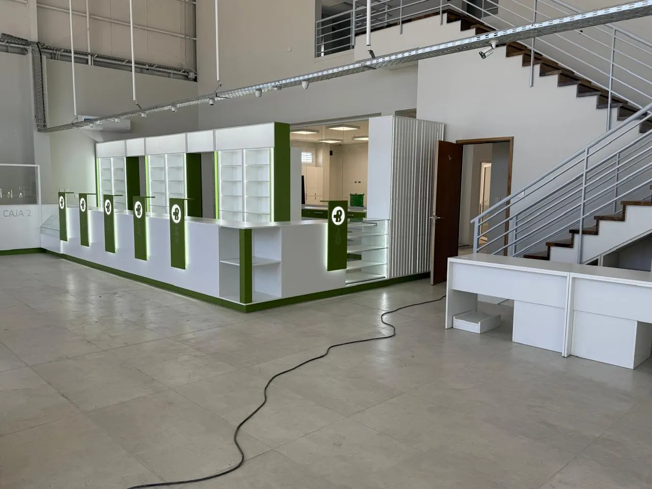 Salón de doble altura con puestos de atención de frente verde y logo institucional, junto a la escalera interna.
