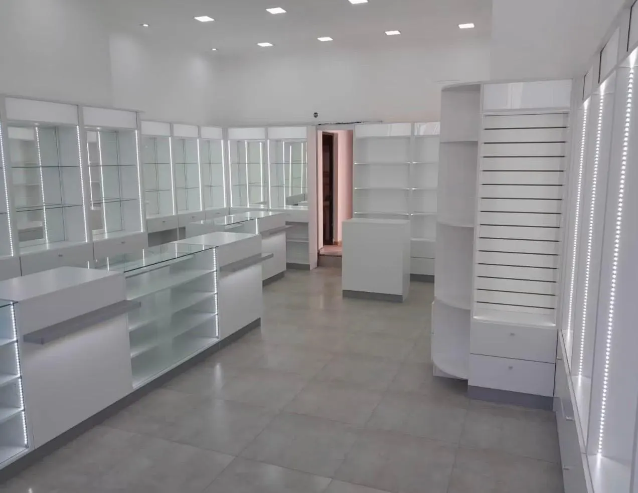 Puestos de atención numerados con cruz farmacéutica y estantería slatwall, sobre piso blanco pulido.