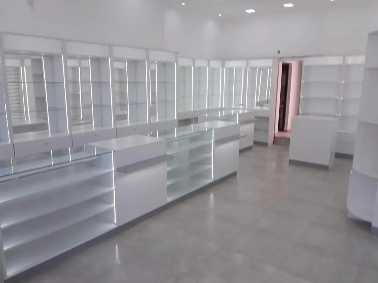 Estantería perimetral con perfiles LED verticales y columnas verdes, junto al sector de oficina vidriado.