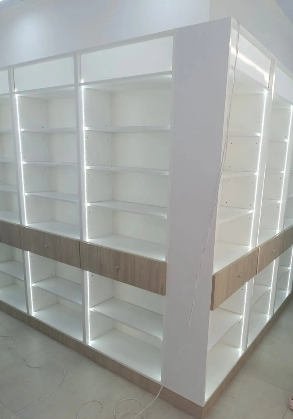 Detalle de estanterías blancas con cajones y perfiles LED integrados en cada módulo.