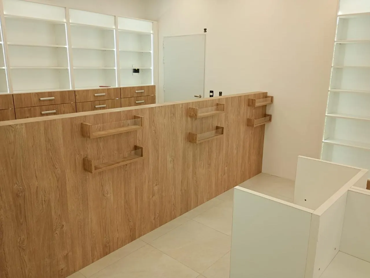 Mostrador de atención con frente en melamina símil madera, repisas voladas y estantería vidriada al fondo.