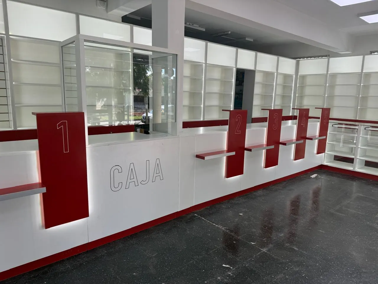 Puestos de atención numerados con frente rojo y sector de cajas, sobre piso oscuro.