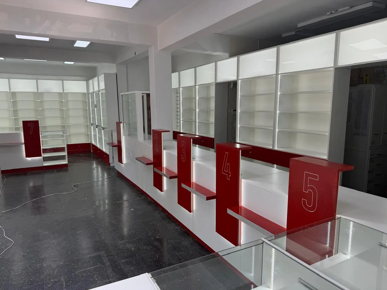 Estantería perimetral con perfiles LED verticales y columnas verdes, junto al sector interno vidriado.