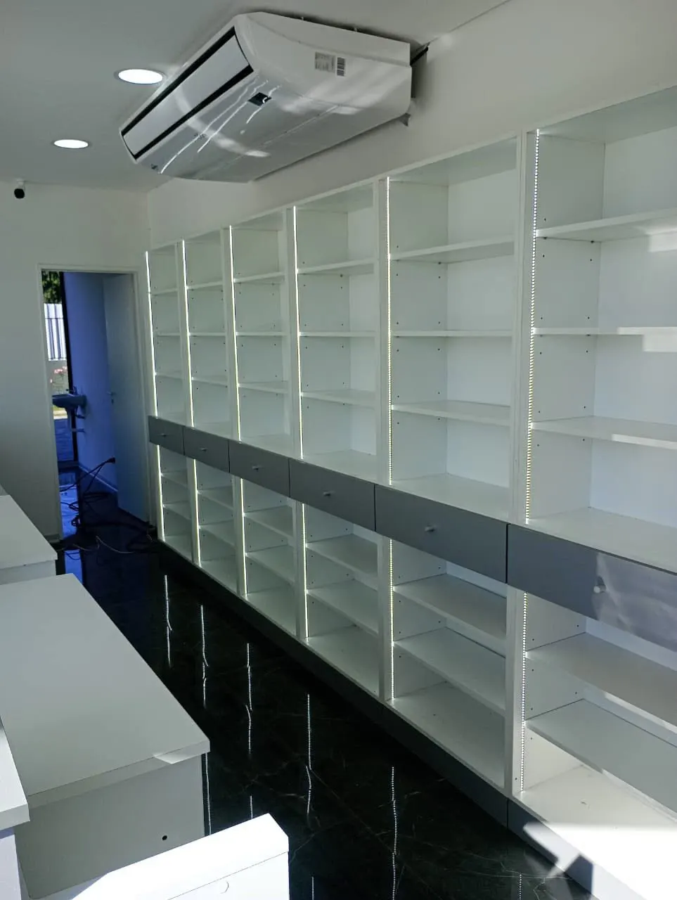 Estantería perimetral blanca de piso a techo con perfil LED verde en la esquina superior.