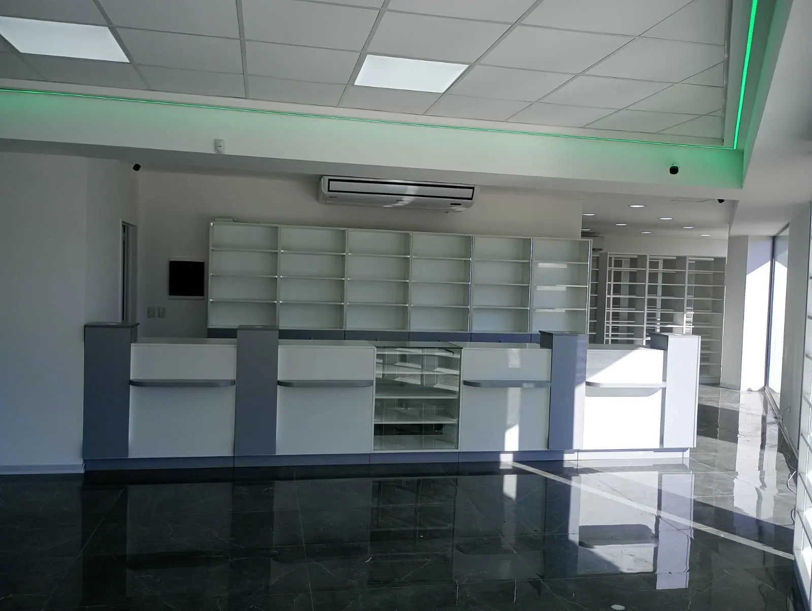 Salón con piso negro, mostradores blancos y perfil LED verde perimetral en el cielorraso.